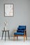 Flowers on wooden table next to blue armchair in grey apartment interior with poster.