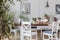 Flowers on wooden table in white cottage dining room interior with posters and chairs. Real photo