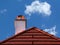 Fluffy white clouds and blue sky above sloped red clay house roof and white chimney