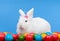 Fluffy white rabbit with pink bow guarding colorful eggs