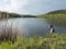 Fly Fisherman angler standing on shore of calm water of forest lake, fish pond Kunraticky rybnik with birch and spruce