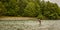 A fly fisherman spey casting while wading in a fast flowing, green, glacial river