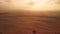 Fly over the desert terrain at sunset, dunes to the horizon.