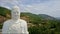 Flycam Approaches Closely to Buddha Statue Head against Hill