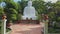 Flycam approaches white buddha statue among in tropical park