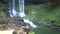 Flycam rises above landscape with waterfall and girl on rock