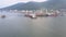 Flycam zooms in boats sailing past pier with port cranes