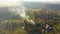 Flying above autumn countryside village with burning dry grass and white smoke