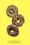 Flying falling levitating floating brown sweet sugar glazed doughnuts,tasty donuts in air on yellow background.Creative