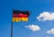 Flying German national flag on pole with blue cloudy and sunny sky