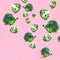 Flying green broccoli slices on a pink background.