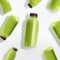 Flying green smoothie or juice bottles pattern on white background, top view