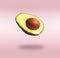 Flying half avocado with seed at pink background with shadow. Concept of food levitation