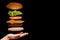Flying ingredients burger or cheeseburger on a small wooden cutting board isolated on a dark background. Burger floating in the