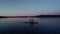 Flying low angle around woman and kids on sup board on calm lake in evening twilight.