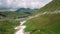 Flying over beautiful mountain valley covered with stones and snow with grass under wonderful hovering clouds from above