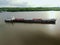 Flying over a large cargo ship with open holds sailing down a calm river surrounded by forest. Carriage of goods by river.