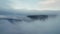 Flying over low hanging clouds with side view of steep rocky mountain cliff in the Scandinavian landscape