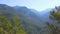 Flying over the mountains covered by green forest on blue sky background. Art. Breathtaking aerial view of green hills