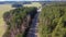 Flying over picturesque road among agricultural fields and pine forest