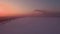 Flying over snow field sunset and lonely chimney-stalk with smoke on the horizon