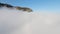 Flying over thick clouds to mountains. Shot. Top view of thick clouds near steep rocky mountains. Beautiful clouds near