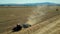 Flying over tractor on cultivated farm field, mountains background, wheat crop