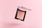 A flying packaging of pink blush on a pink background. Product of the beauty industry, female accessory of cosmetics levitate in