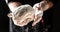 Flying pizza dough with flour scattering in a freeze motion of a cloud of flour midair on black. Cook hands kneading dough. copy