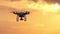 A flying quadracopter with four rotating blades at sunset in slo-mo