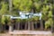 A flying quadrocopter against the background of trees in cloudy weather takes pictures of the surface of the earth