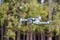 A flying quadrocopter against the background of trees in cloudy weather takes pictures of the surface of the earth