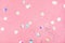 Flying silver holographic confetti on pastel pink background.