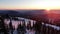Flying through snow-covered treetops and over ski lift cabins at sunset against background of mountains in rays of