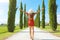 Flying in Tuscany concept. Young woman walking in beautiful and idyllic landscape of a lane of cypresses in the Italian