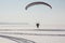 The flying-up person on a motorized paraglider against a snow surface of the river