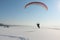 The flying-up person on a motorized paraglider against a snow surface of the river