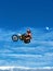 FMX motorbike rider completing stunts against the backdrop of a blue sky with clouds and the moon