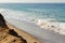 Foaming fading wave on sandy shoreline, wave cresting, foaming backwash, sandy cliff rise