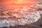 Foamy sea water in orange sun flare. Relaxing sea wave surf over seashore.
