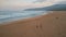 Foamy sea waves rolling on sandy beach drone view. Surfers walking seashore