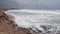 Foamy stormy waves roll on shallow sand beach with rocks