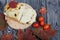 Focaccia bread with olives and sun-dried tomatoes. Several red tomatoes and dried autumn leaves are nearby. On pine boards