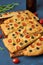 Focaccia, pizza, italian flat bread with tomatoes, olives and rosemary. Dark blue background, side view