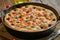 Focaccia, pizza in skillet. Close up italian flat bread with tomatoes, olives and rosemary. Side view, wooden table