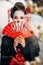 Focus of beautiful geisha in black kimono with flowers in hair holding hand fan in front of face and sakura branches in