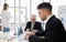 Focus on Business manager wearing eyeglass writing on paper and staff sitting typing and seeing on laptop near colour pens. Woman