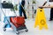 Focus of cleaning trolley near wet floor sign and multiethnic cleaners working in office