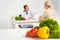 Focus of dietitian in white coat and patient at table and fresh vegetables on foreground