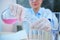 Focus on a glass laboratory flask in the hands of blurred scientist pouring liquid through a lab funnel into a test tube